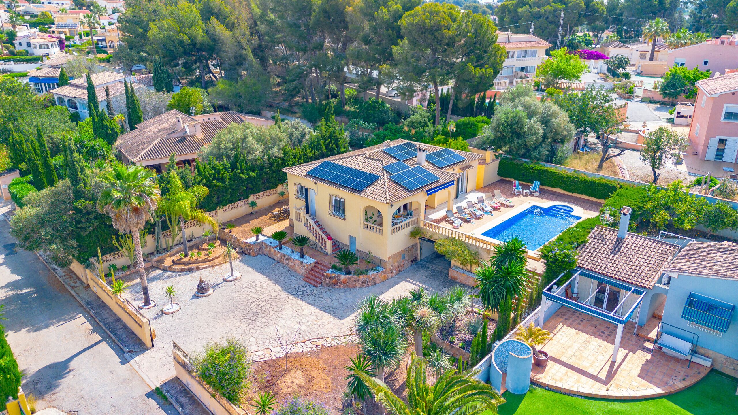 Vista aérea de una propiedad residencial con piscina, paneles solares y un jardín bien cuidado.