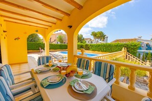 Zona pranzo con tavolo apparecchiato per quattro, posti a sedere all'aperto e vista su piscina e giardino.