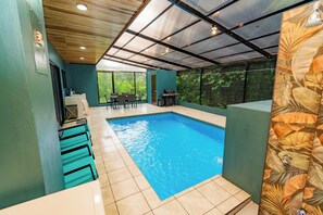 Une piscine dont le sol est carrelé, entourée de murs aux tons verts et surmontée d’un plafond en bois.