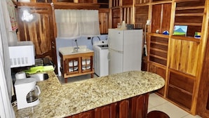 Una cucina compatta con mobili in legno, un piano di lavoro in granito, un lavandino piccolo, un frigorifero e una macchina da caffè.