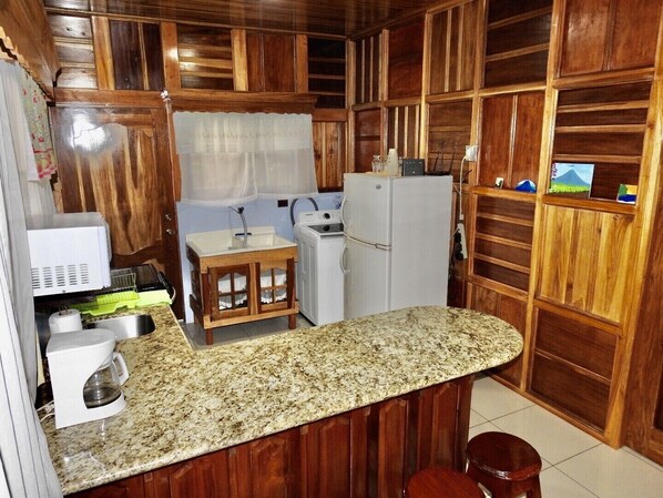 A compact kitchen with wooden cabinets, a granite countertop, a small sink, a refrigerator, and a coffee maker. - Bosque Alto House (La Fortuna)
