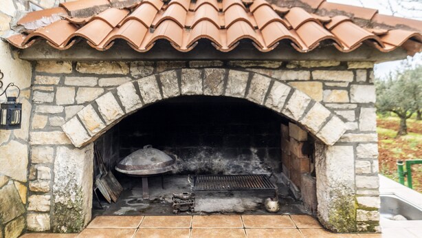 A stone-built outdoor pizza oven with a tiled roof and a chimney.