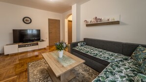 A modern living room with a flat-screen TV, wooden coffee table, patterned sofa, and a decorative shelf.