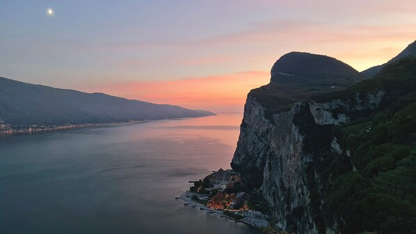 A coastal town with a prominent cliff, a calm sea, and a visible moon. - Campione Giulia Exclusive Lakefront (Campione del Garda)
