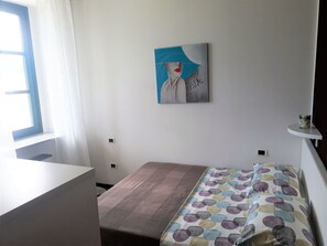 A room with a bed, a desk, a window with curtains, a wall-mounted painting, and a small shelf. - Campione Giulia Exclusive Lakefront (Campione del Garda)