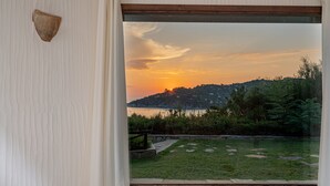 Une vue à travers une fenêtre sur un coucher de soleil au-dessus d’une zone herbeuse, avec un chemin de pierres et une clôture en bois.