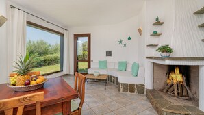 Un coin repas avec une table et des chaises en bois, un panier de fruits et une vue sur l’extérieur grâce à une grande fenêtre.