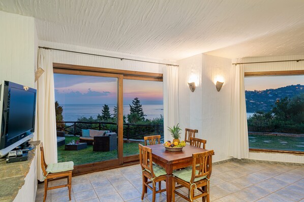 A dining area with a table and chairs, a television, and a view of the ocean.