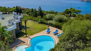 Une piscine avec des chaises longues, une terrasse en pierre et une vue sur la mer.