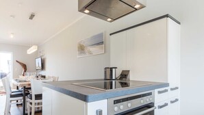 A modern kitchen with a built-in stove, oven, and a dining area with a table and chairs. - Fehmarn - Fehmarn in List on Sylt (List)