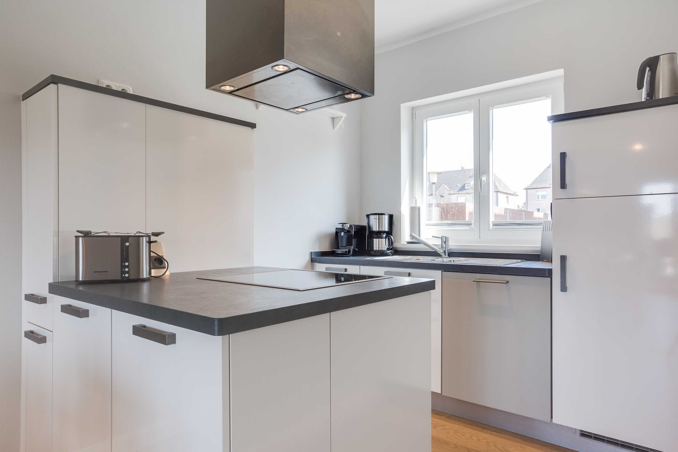 Une cuisine moderne avec des meubles blancs, un îlot central, une fenêtre offrant une belle vue et une cuisinière intégrée.
