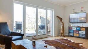 A modern living room with a large sliding glass door, a leather sofa, a wooden coffee table, a cowhide rug, a wooden cabinet with drawers, and a flat-screen TV mounted on the wall. - Fehmarn - Fehmarn in List on Sylt (List)