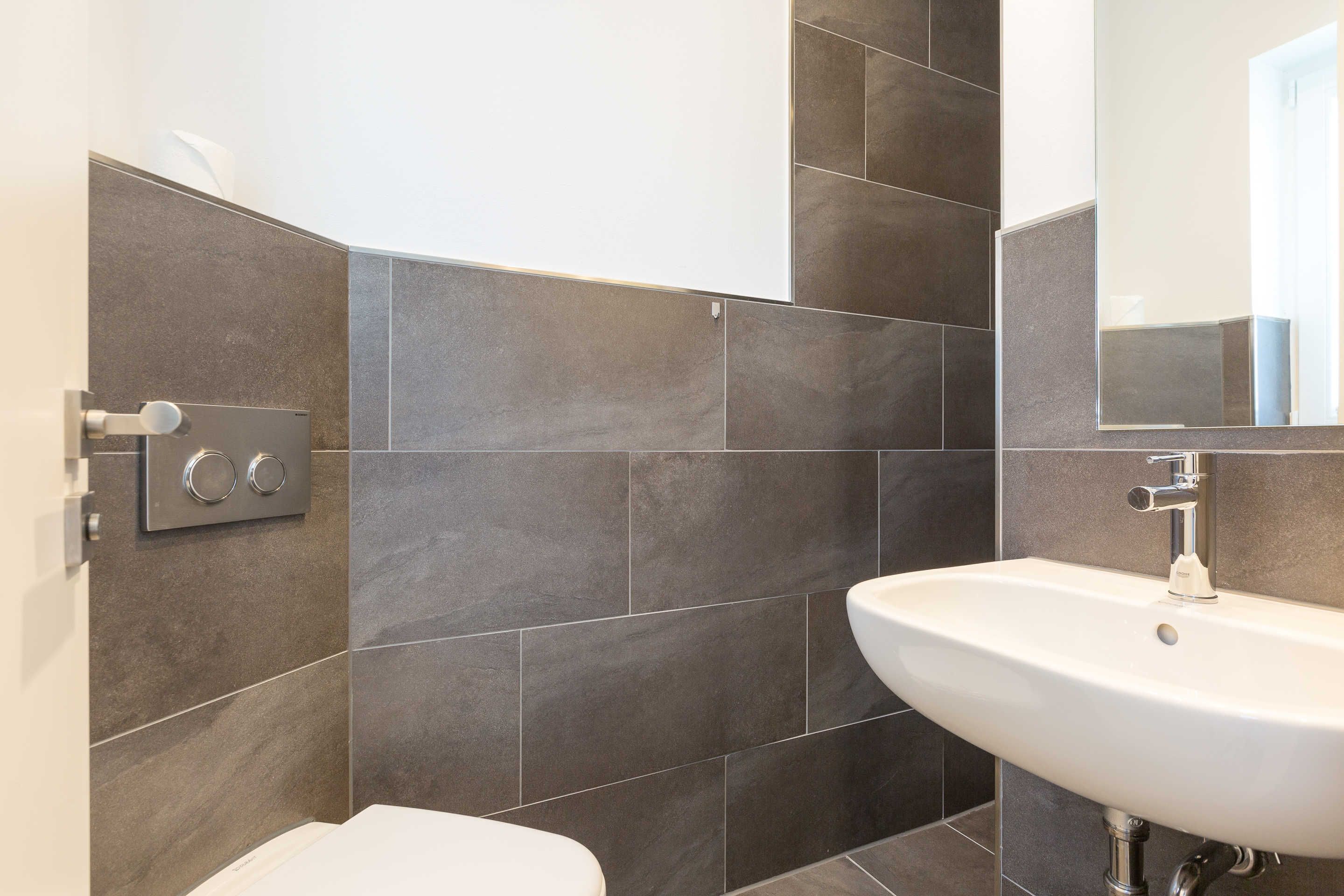 A bathroom with a white sink, dark tiled walls, and a mirror.