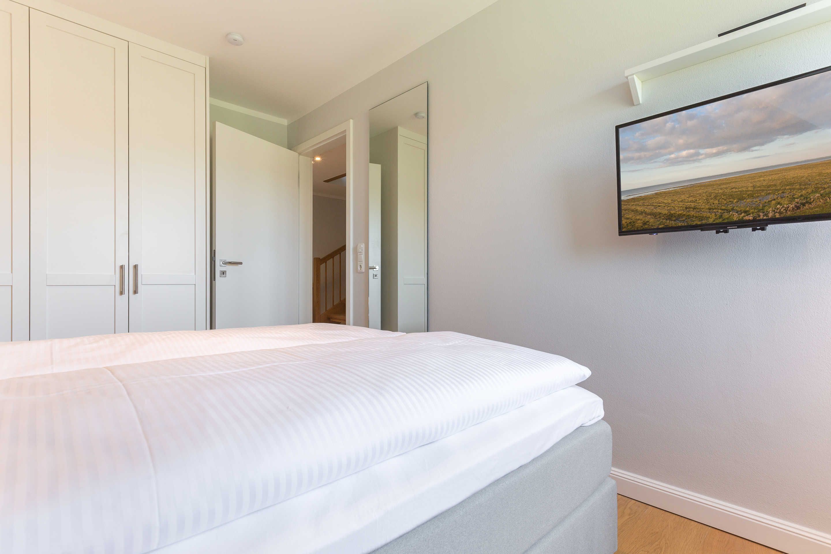 A bedroom with a bed, a TV mounted on the wall, and a door leading to another room.
