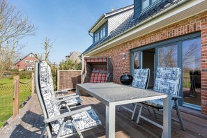 A patio with a table and chairs, a barbecue grill, and a glass door leading to a brick building.