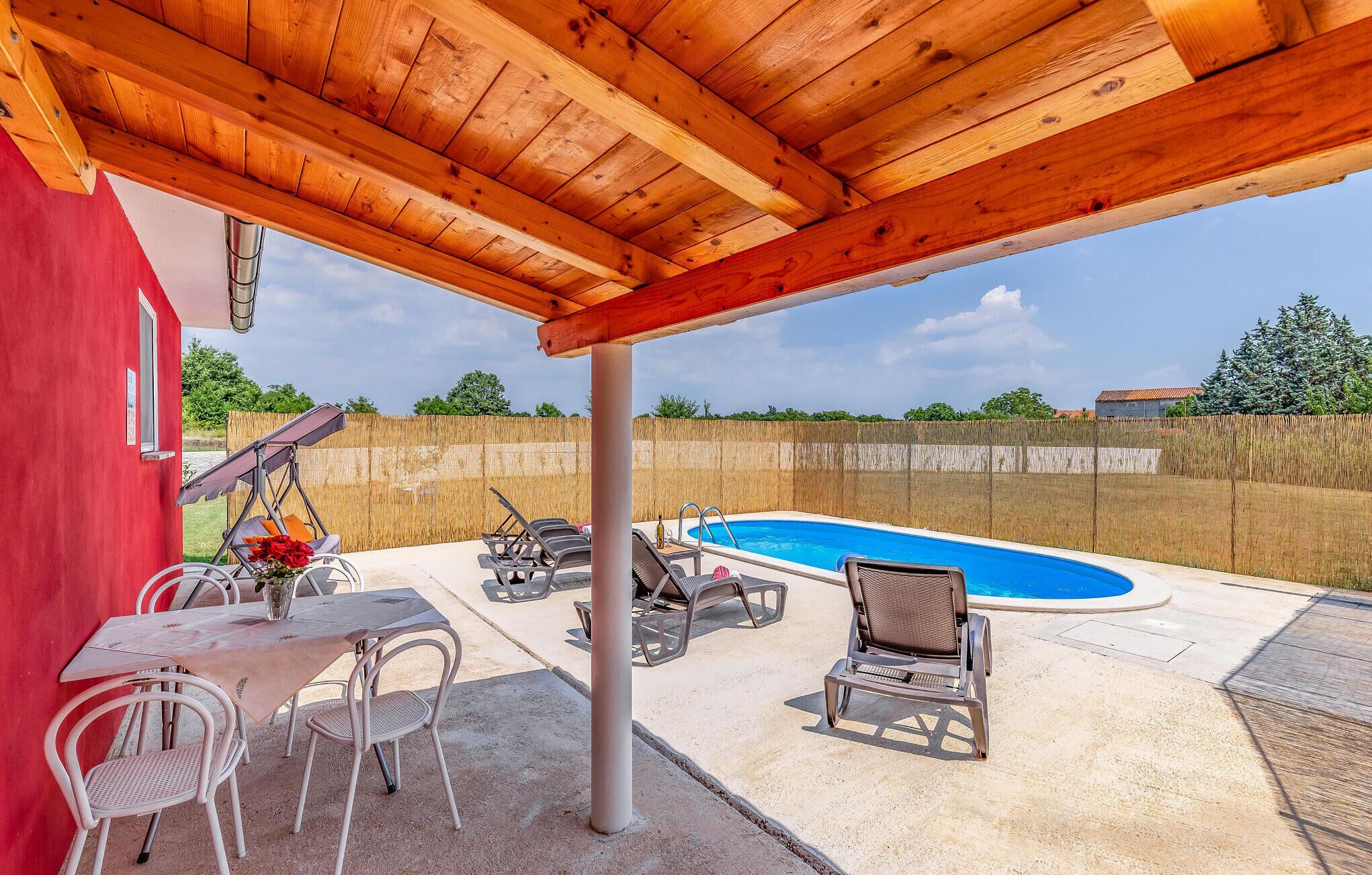 Ein überdachter Außenbereich mit Pool, Liegestühlen und einem Tisch mit Stühlen.