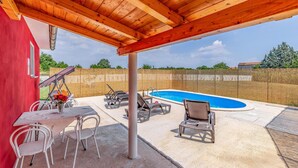 Uma área externa coberta com piscina, espreguiçadeiras e uma mesa com cadeiras.