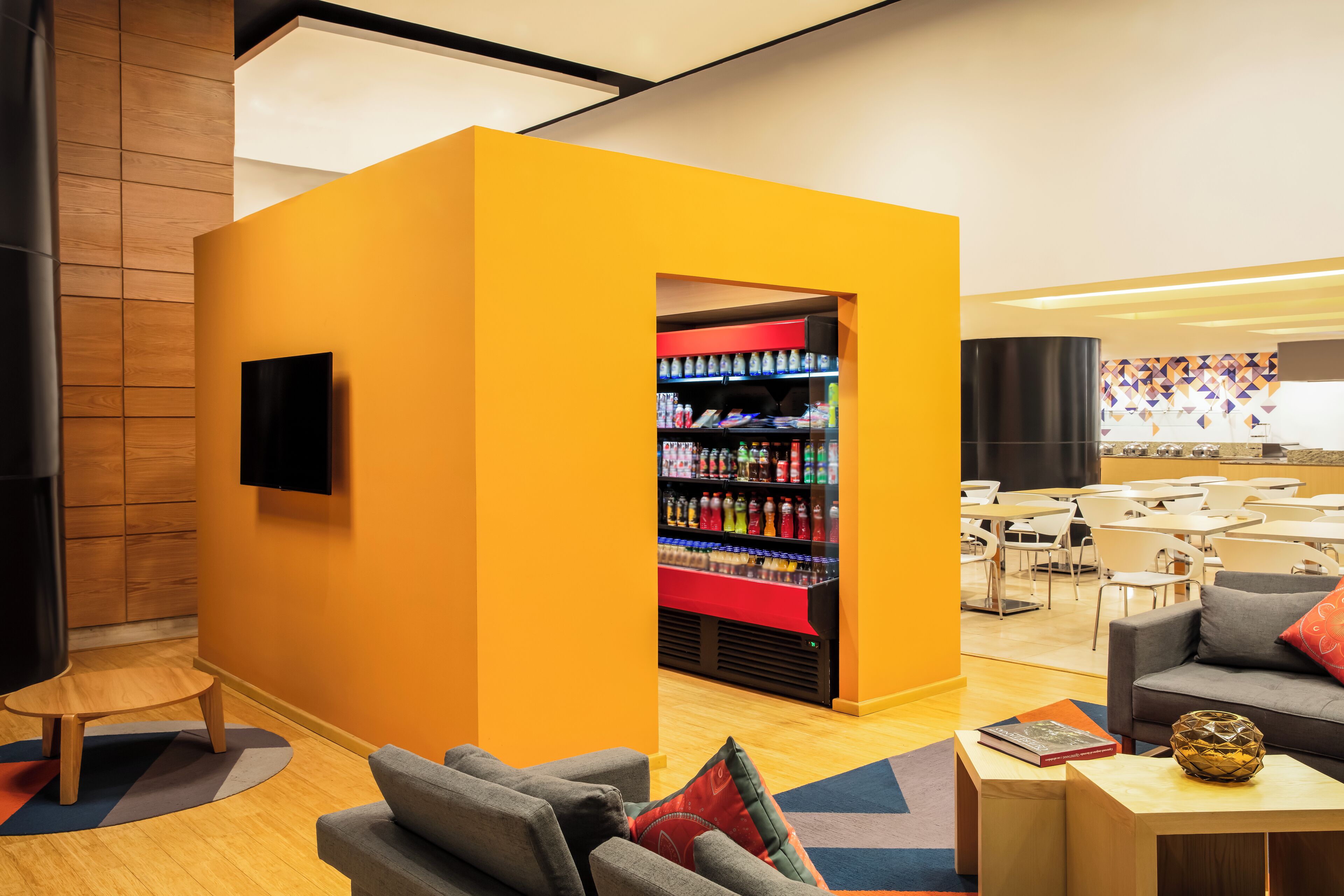 A modern lounge area with a yellow accent wall, a beverage kiosk, and seating arrangements.