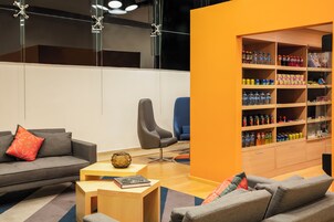 Una sala de estar moderna con sofá, sillón y mesa de centro. Se observa una estantería llena de diversos objetos.