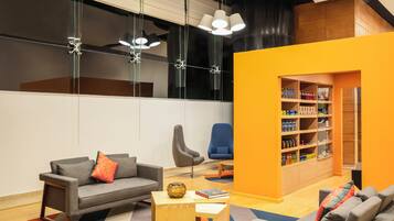 A modern living room with a grey sofa, a blue armchair, and a wooden coffee table. There is a bookshelf filled with various items and a large window with a view of the outside.