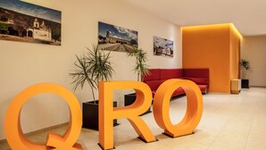 A lobby with large orange letters spelling "QRO", a red sofa, and two potted plants. - Fiesta Inn Express Queretaro Constituyentes (Querétaro)