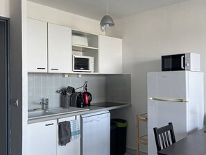 Una cocina compacta con armarios blancos, un microondas, un hervidor y un refrigerador.