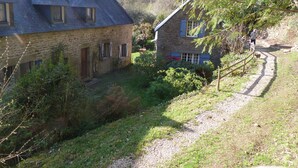A stone house with a sloped roof, a small garden, and a gravel path leading to a wooden bridge. - Concarneau, Former Mill of Kérangoc, in the countryside, near the ocean, Wifi (Melgven)