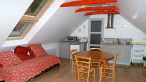 A cozy loft bedroom with a sloped ceiling, a wooden dining table, and a red floral sofa. - Concarneau, Former Mill of Kérangoc, in the countryside, near the ocean, Wifi (Melgven)