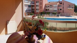 A balcony with a flower vase, a pool, and a pink building in the background. - Cozy Studio-Cabin, Pool Access, 200m from Beach, Sleeps 4 - Argelès-sur-Mer (Argelès-sur-Mer)