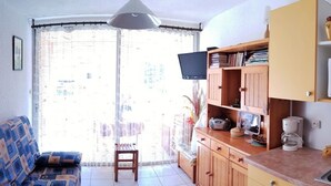 A compact living space with a sofa, a small table, a television, and a kitchenette. - Cozy Studio-Cabin, Pool Access, 200m from Beach, Sleeps 4 - Argelès-sur-Mer (Argelès-sur-Mer)