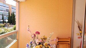 A room with a large window, a round table with a vase of flowers, and a view of buildings and trees outside. - Cozy Studio-Cabin, Pool Access, 200m from Beach, Sleeps 4 - Argelès-sur-Mer (Argelès-sur-Mer)