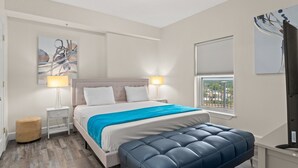 Ein Schlafzimmer mit Bett, Nachttischlampen, einem Fenster mit Blick, einem Bild an der Wand und einem kleinen Hocker.