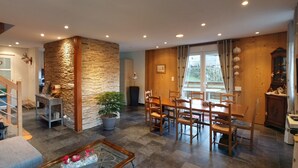 A spacious living area with a dining table and chairs, a staircase, and a stone accent wall. - Magnificent chalet in Hohrod/Munster Alsace with panoramic south-facing view  (Hohrod)