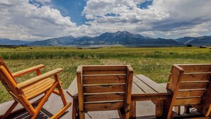 A wooden table and two wooden chairs in a grassy field with mountains in the background. - Yellowstone Trail Lodge · Yellowstone National park (Emigrant)