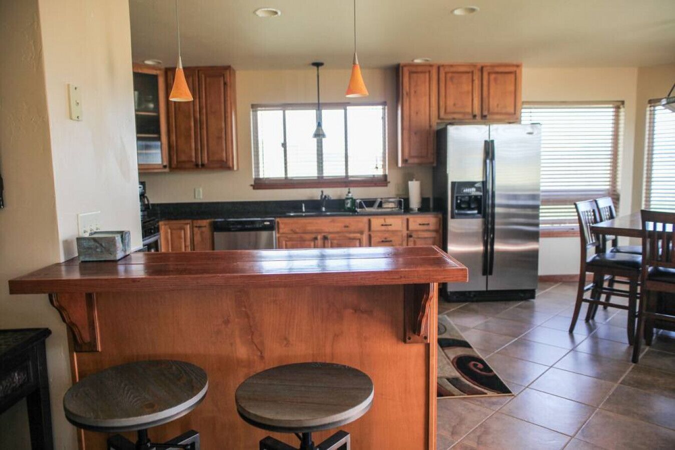 Una cocina con armarios de madera, un refrigerador de acero inoxidable y una isla central con taburetes.