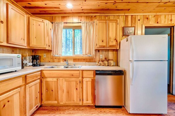 A wooden cabin kitchen with a microwave, coffee maker, sink, and a dishwasher.