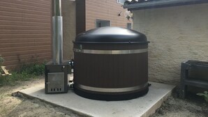 A cylindrical outdoor cooking unit with a chimney, placed on a concrete platform next to a building with a tiled roof and a window. - Beautiful house 170 m2, heated and covered swimming pool, jacuzzi, classified 4 stars. (Laruscade)