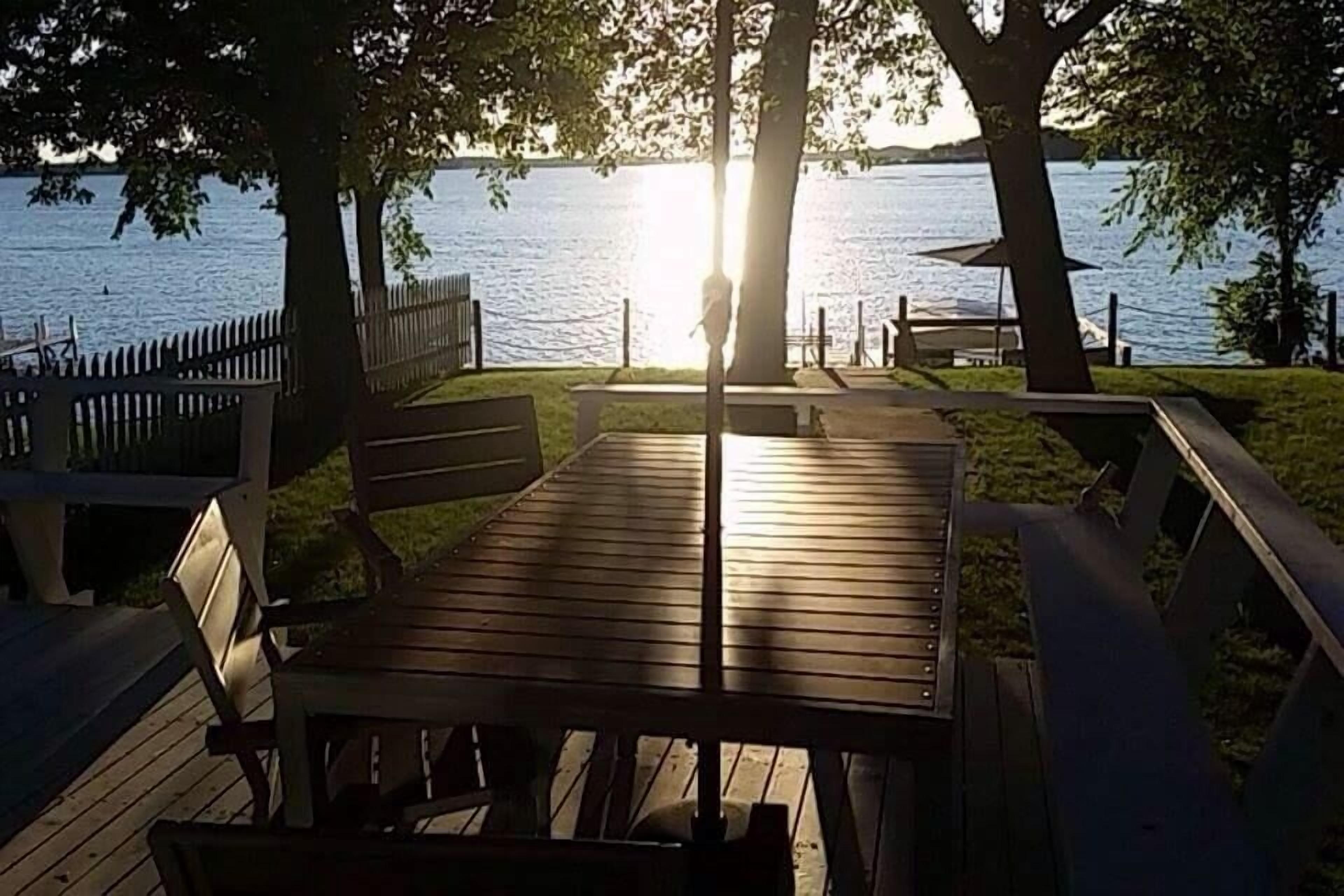 Une terrasse en bois avec une table et des bancs, donnant sur une étendue d’eau.