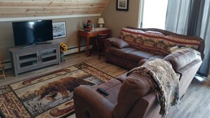 Una sala de estar con techo de madera, televisor, sofá, mesa de centro y alfombra con estampado de animales.