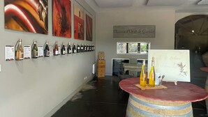 Une salle de dégustation de vins avec une table en forme de barrique où sont exposées des bouteilles, un mur orné d’œuvres d’art encadrées et une enseigne indiquant « Château d’Or et les Gouves ».