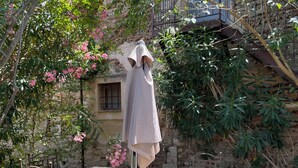 Un bâtiment en pierre doté d’un balcon, entouré d’une végétation luxuriante et de plantes en fleurs.