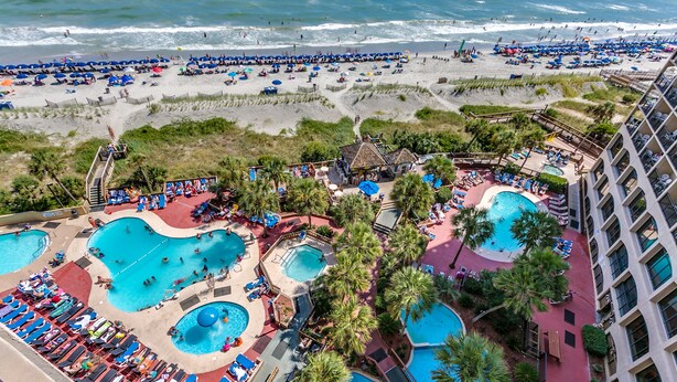 Ein Resort mit mehreren Swimmingpools, einem Strandbereich und Meerblick.