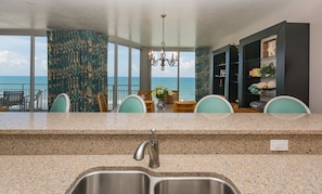 A kitchen with a granite countertop, stainless steel sink, and a view of the ocean through large windows. - Luxury Oceanfront SR701 with Wraparound Balcony Pet Friendly (New Smyrna Beach)