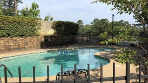 Une piscine avec un mur en pierre, une clôture en métal et une table avec des chaises.