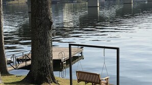 Un parc avec une aire de jeux comprenant des balançoires et une jetée au bord d’un lac paisible, avec un pont en arrière-plan.