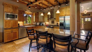 Una cocina amplia con armarios de madera, una isla grande con taburetes de bar, electrodomésticos de acero inoxidable y un techo alto con vigas a la vista.