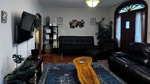 A living room with a black sofa, a wooden coffee table, a TV mounted on the wall, and a ceiling light fixture. - Cozy family home, close to all things Hershey and Central Pennsylvania... (Palmyra)