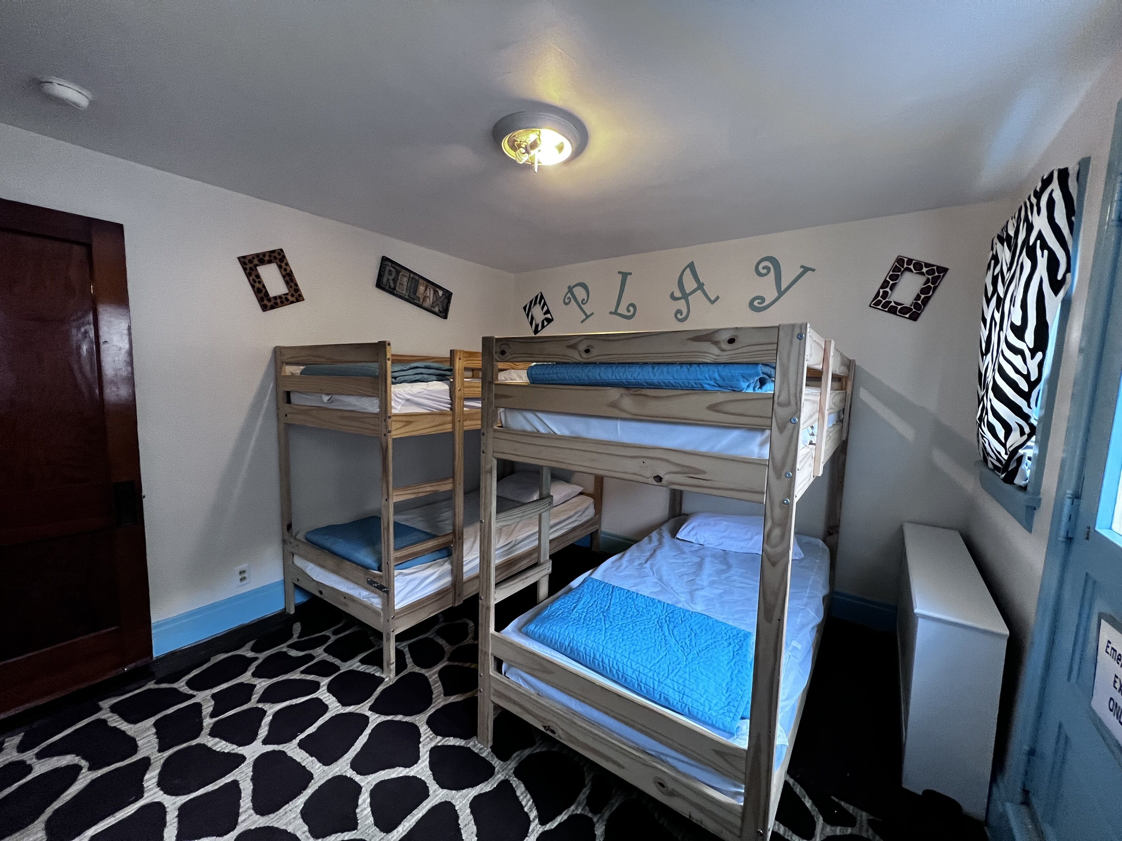 A room with bunk beds, a giraffe-patterned rug, and wall decorations including a zebra print and a nameplate.