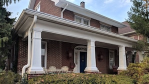A two-story brick house with a covered porch supported by white columns, a blue door, and a small front yard with a hedge. - Cozy family home, close to all things Hershey and Central Pennsylvania... (Palmyra)