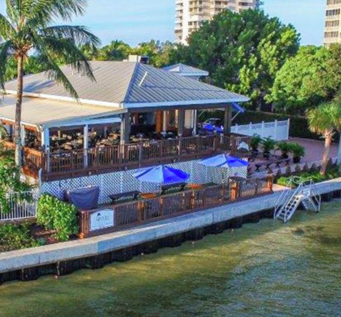 Ein Restaurant am Wasserufer mit Terrassensitzgelegenheiten, einem überdachten Bereich und Blick auf das Wasser.